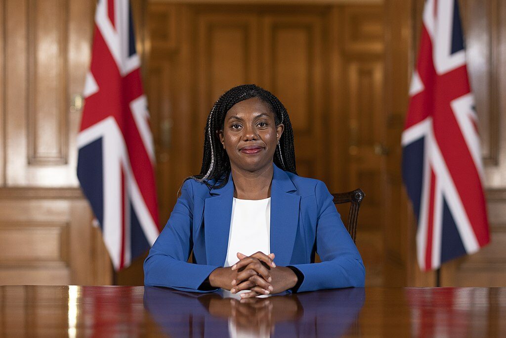 Kemi Badenoch sat at a table with Union Jack flags behind her