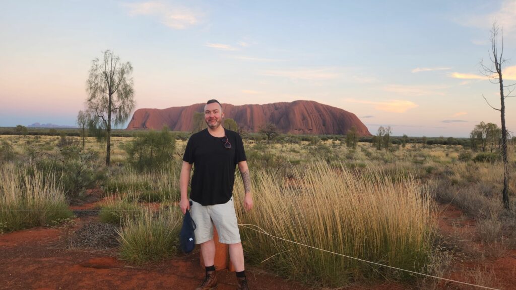 A man stands in front of Uluru smiling