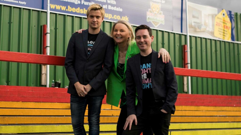 Threee people on a rainbow coloured rugby stand