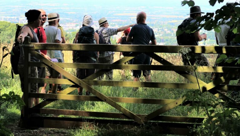 A group of people stand in a field by a wooden gate as they hike together