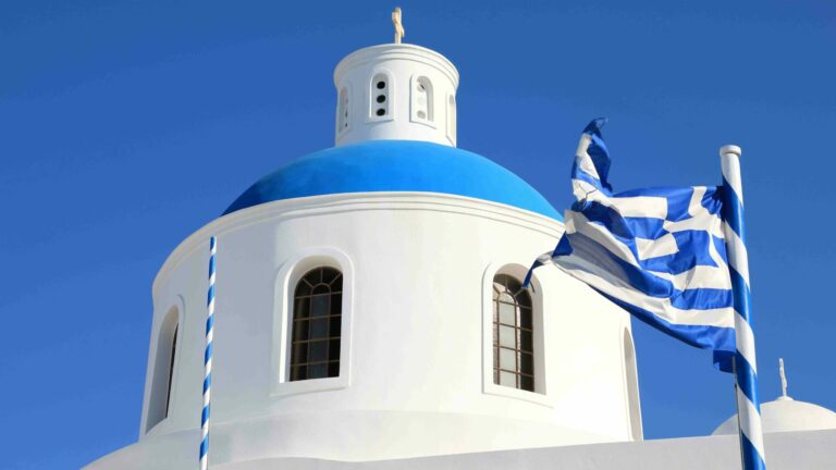 Greek flag billowing in front of a white building