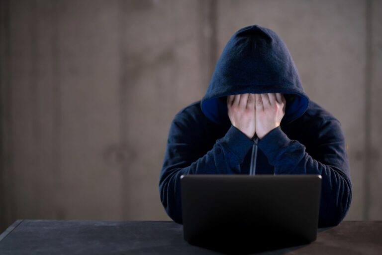 Stock photo of a man sitting by an open laptop with his hands covering his eyes