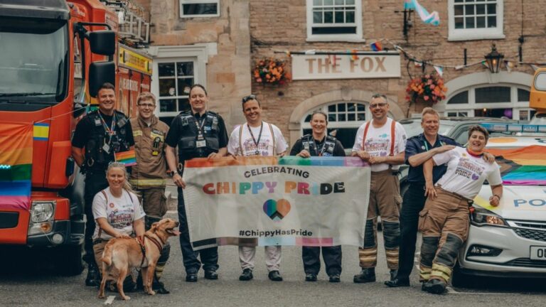 A group of firefighters and police officers holding up a Chippy Pride flag