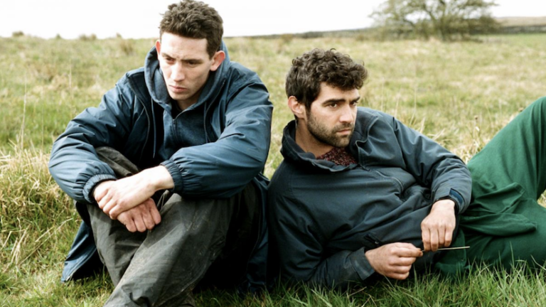 The stars of God's Own Country sitting on a farm in a field
