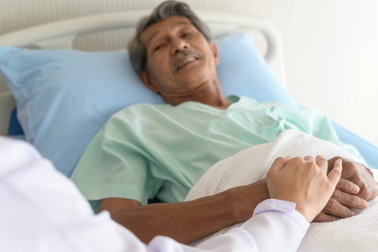 Stock image of a man in a hospital bed with a doctor holding his hand