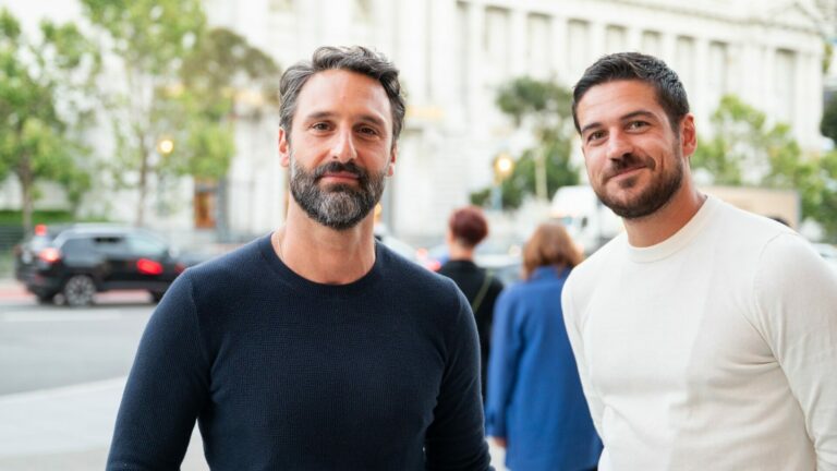 Marco Calvani, in a black top, and Marco Pigossi, in a white top, standing on a street