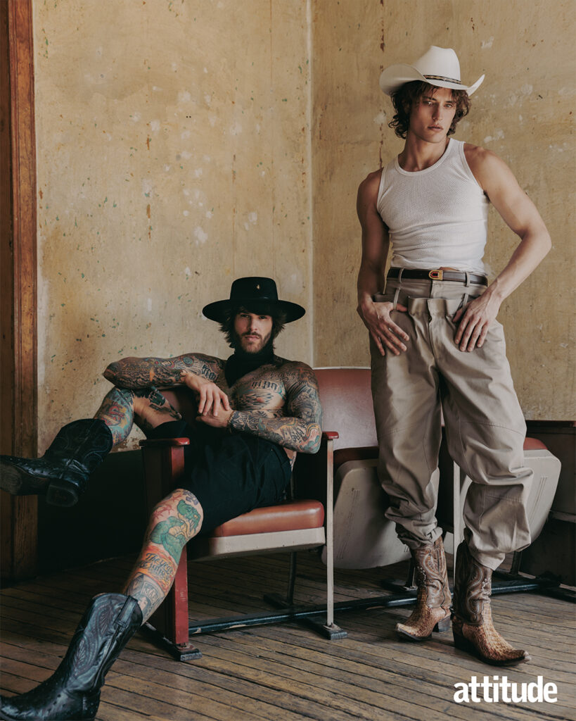 One model sits in black wide brim hat, shorts and cowboy boots while the other model stands next to him in off white cowboy hat, white vest, beige cargo trousers and brown cowboy boots