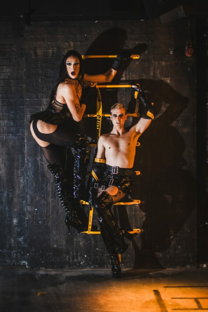two pvc-clad dancers leaning against a wall