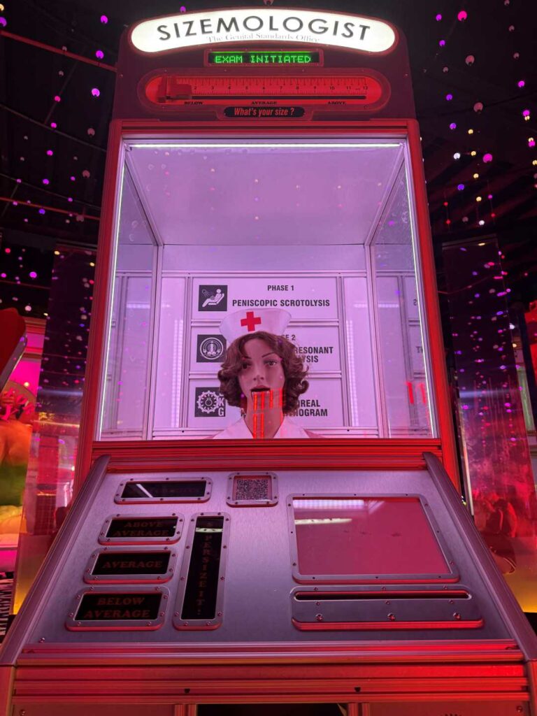 A dummy's head displayed inside a brightly lit, pink-themed booth with playful signage and buttons below.