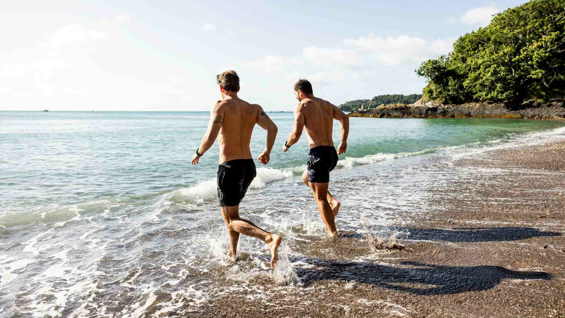Two men in shorts running towards the sea in Jersey
