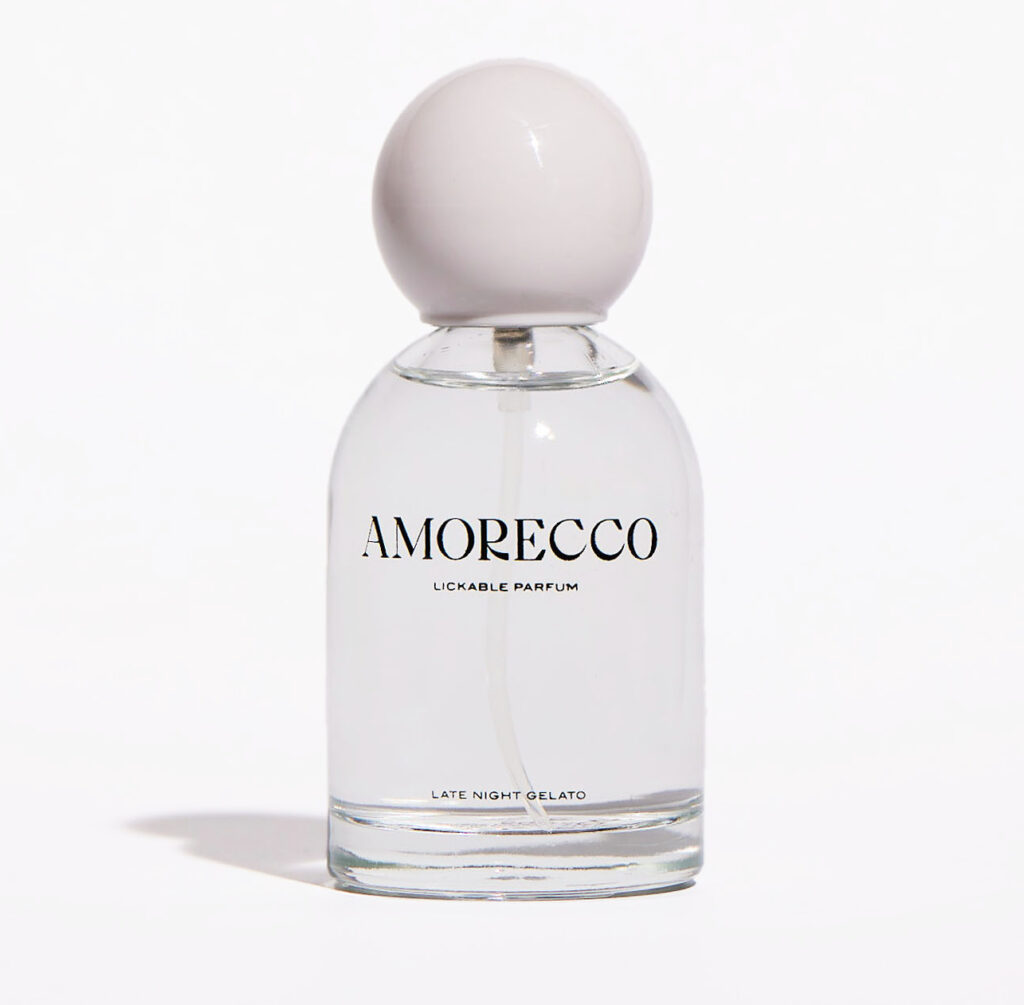 Clear glass bottle of AMORECCO lickable parfum, with a white spherical cap and minimalist black text reading "Late Night Gelato."