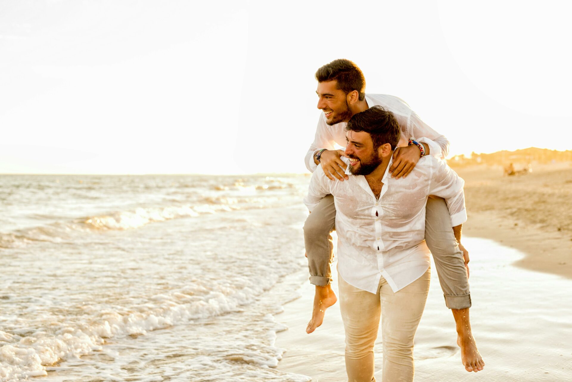 One man giving another man a piggyback ride on the beach