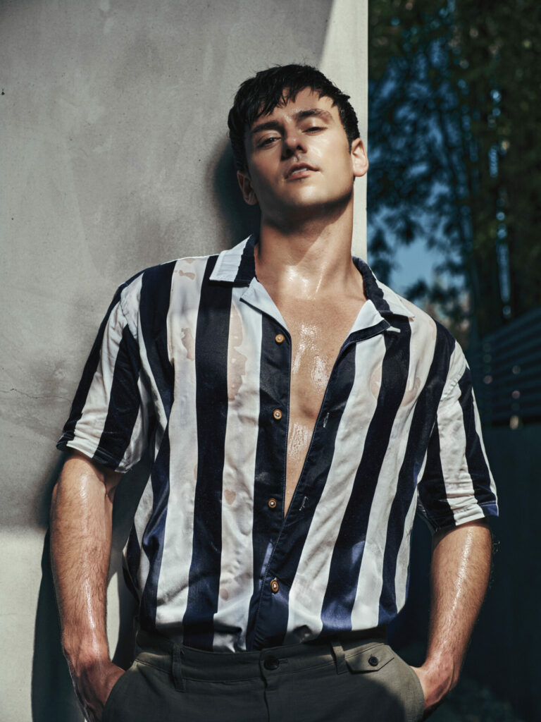 Tom Daley poses with wet skin in navy and white stripe shirt and khaki trousers