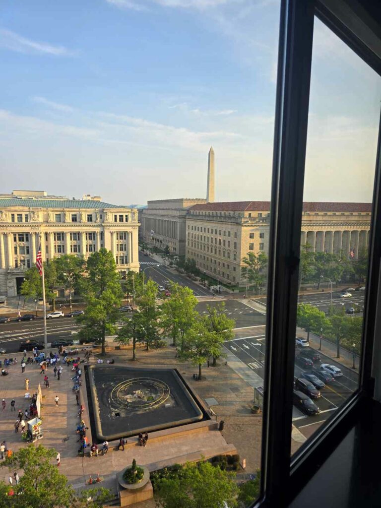 A view out of a hotel window with a view of the Washington Monument behind builidings