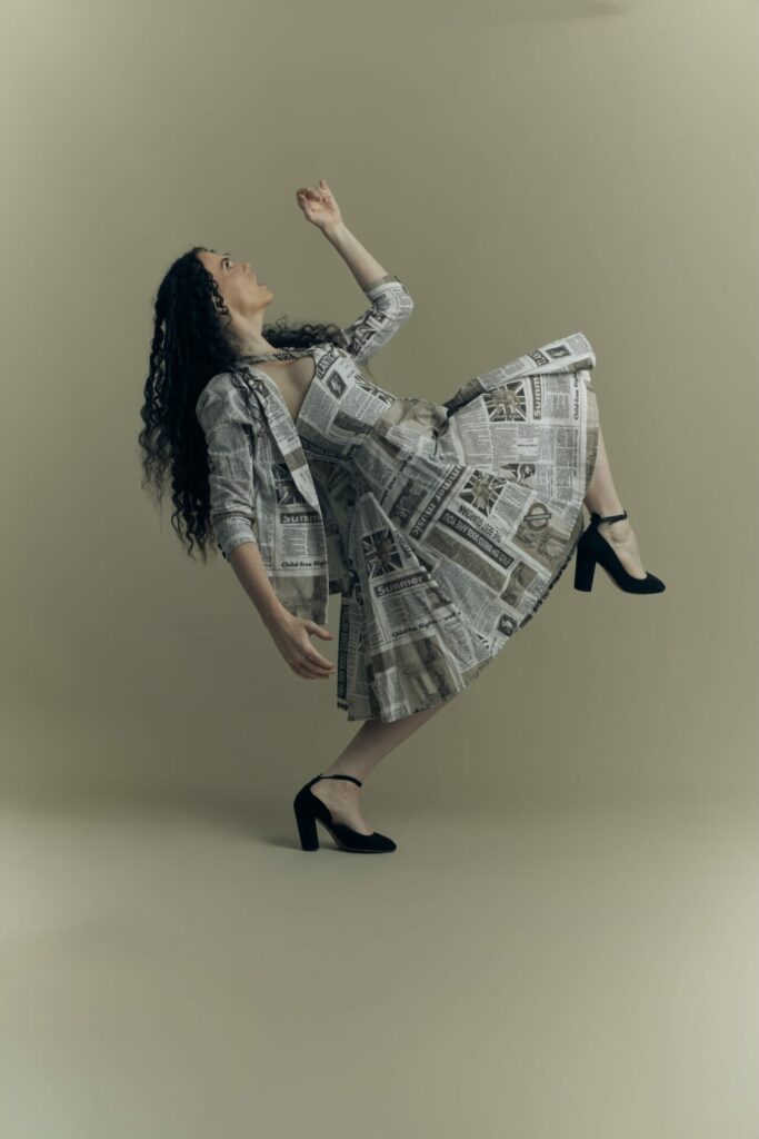 Jordan standing on one foot in a news print dress - attitude photoshoot