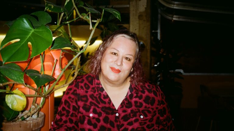 Alana S. Portero wearing a deep red cheetah print top, with curly hair and light red lipstick