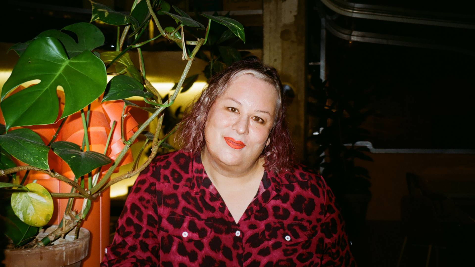 Alana S. Portero wearing a deep red cheetah print top, with curly hair and light red lipstick