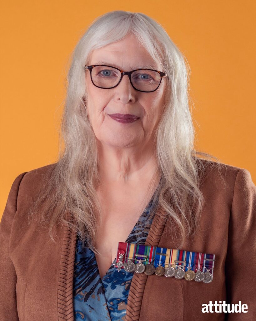 Caroline, a close up head and shoulders, against an orange backdrop wearing a brown jacket and blue top with medals on show and hair down