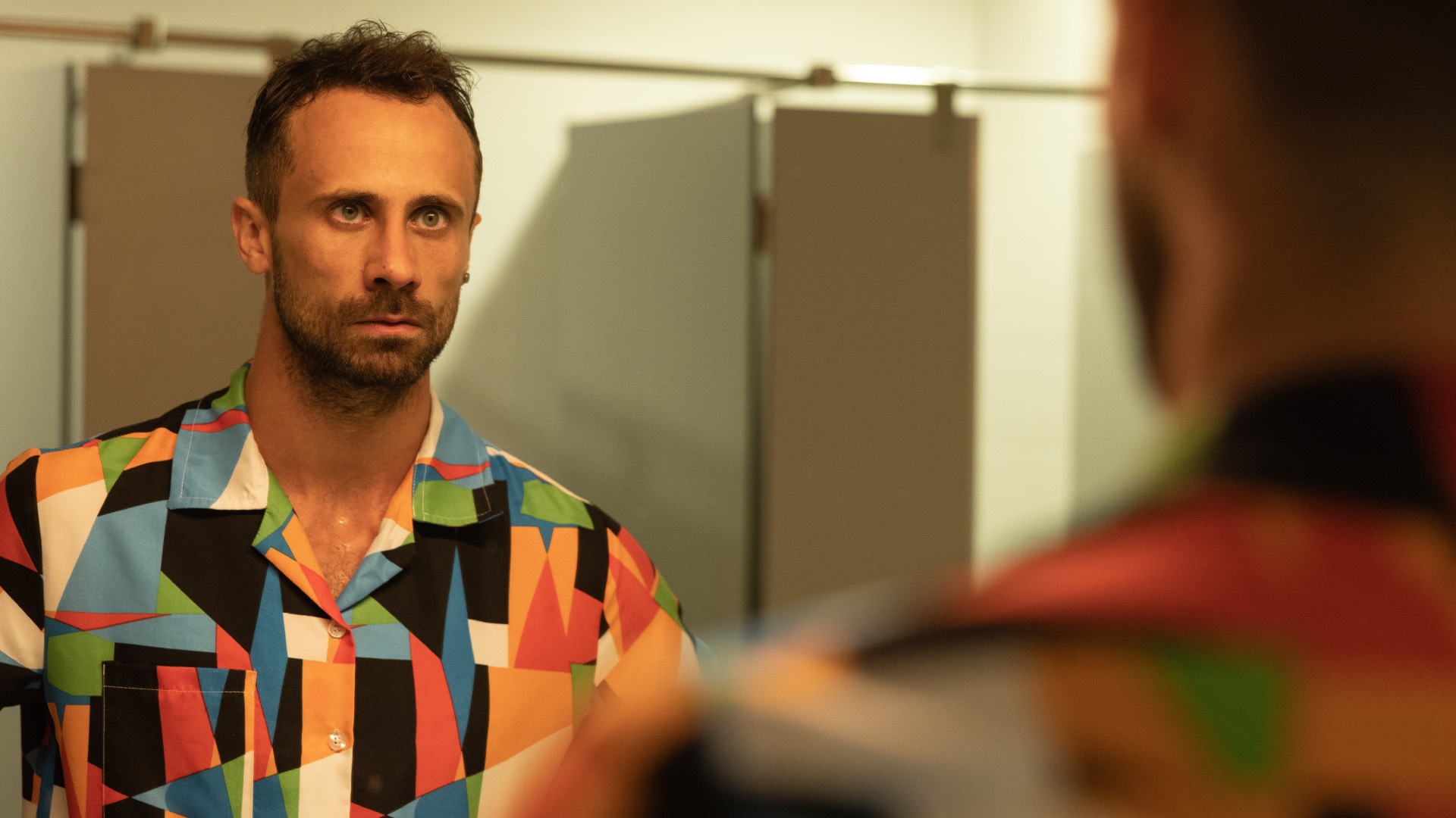 Oriol Pla in I, Addict, in a colourful shirt looking into a mirror
