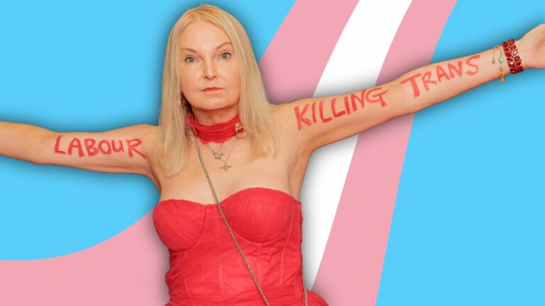 India Willoughby in a red dress standing with arms outstretched in front of a trans pride flag background with the words 'LABOUR KILLING TRANS' written on her arms