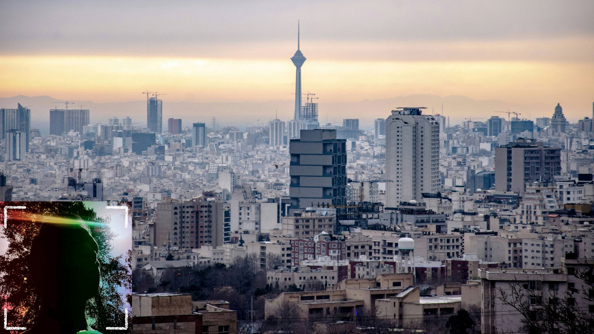 A portrait image of a man's darkened face sitting over a view of the Tehran skyline