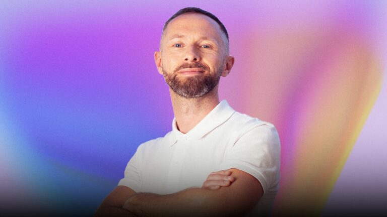 A smiling man with a white polo shirt against a colourful gradient backdrop