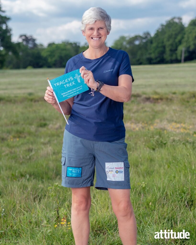 Tracey in blue, standing in a field, holding a flag reading 'Traceys Trek'