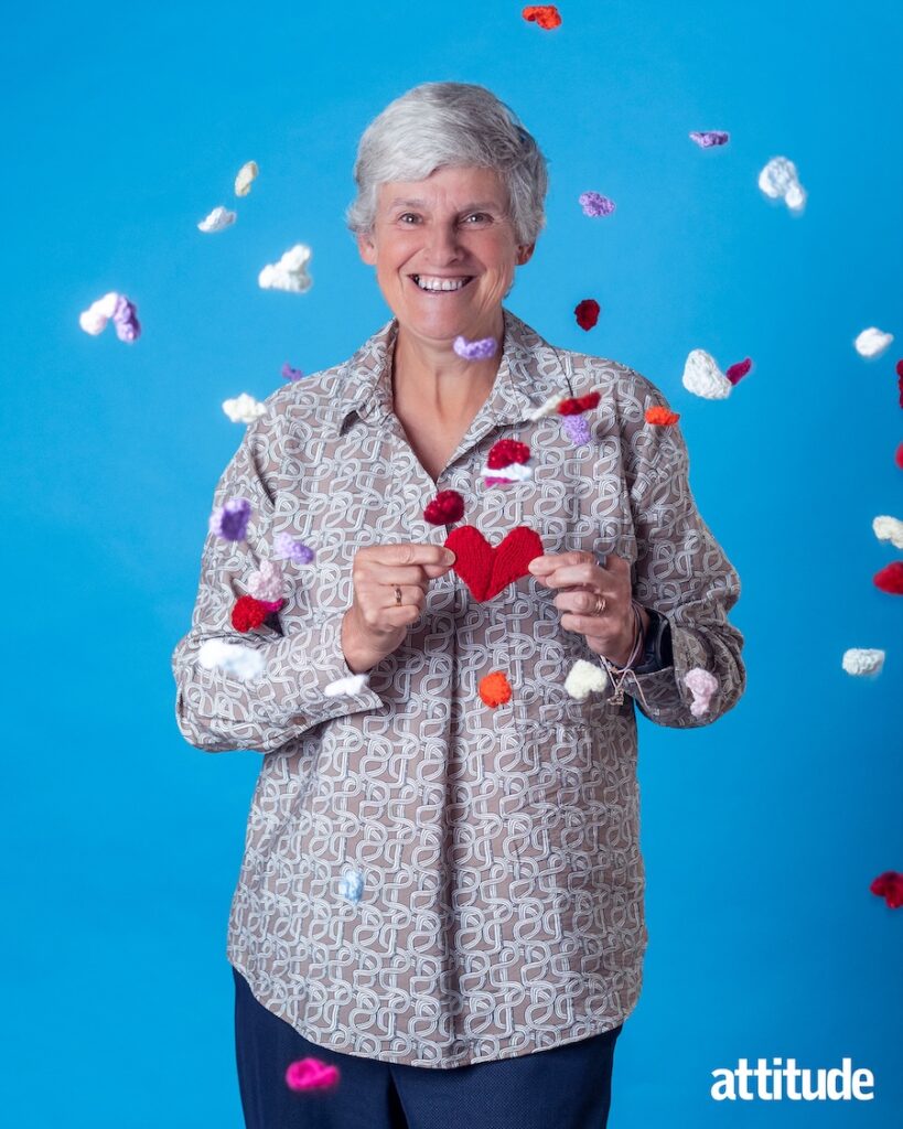 Head and shoulders of Tracey Howe against a blue backdrop, with knitted multi-coloured hearts being thrown in the air