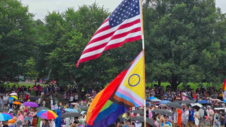 Crowd at a Pride event with US and LGBTQ+ flags flying in the foreground