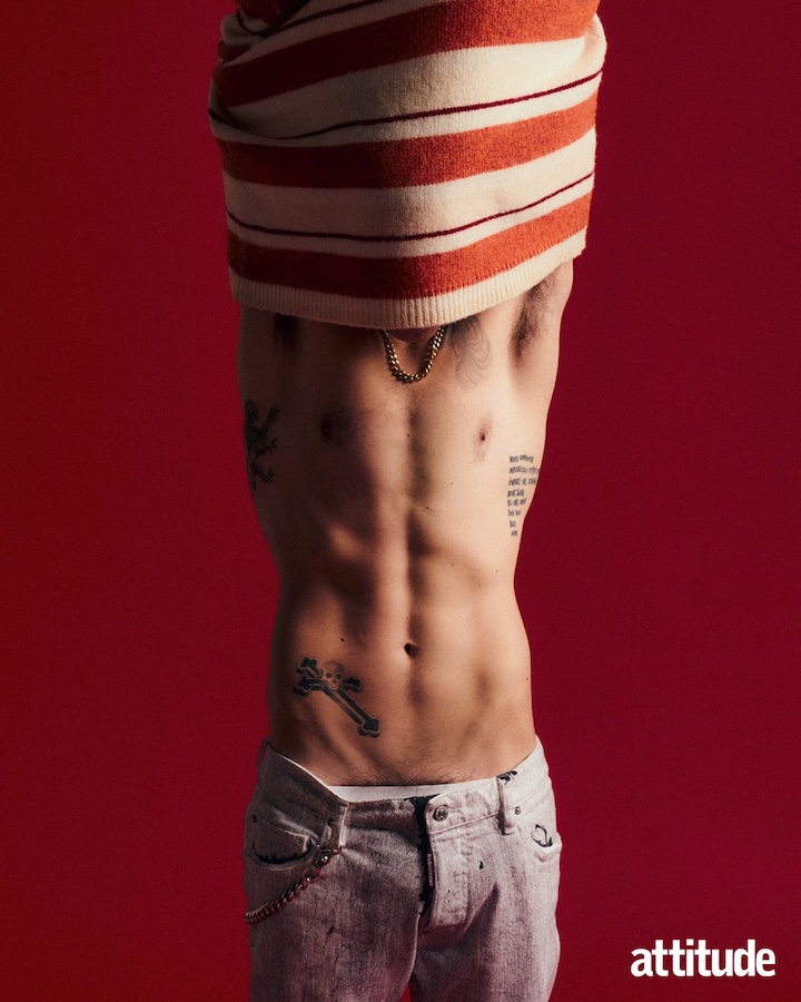 yungblud taking his top off, face covered by orange and white striped jumper