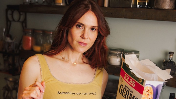Kate Nash wearing a yellow vest with the words 'Sunshine on my mind' written across her chest, holding a box of cereal.