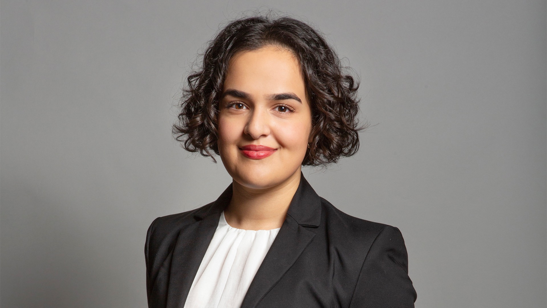 a head and shoulders shot of Nadia in white top and grey blazer with hair down