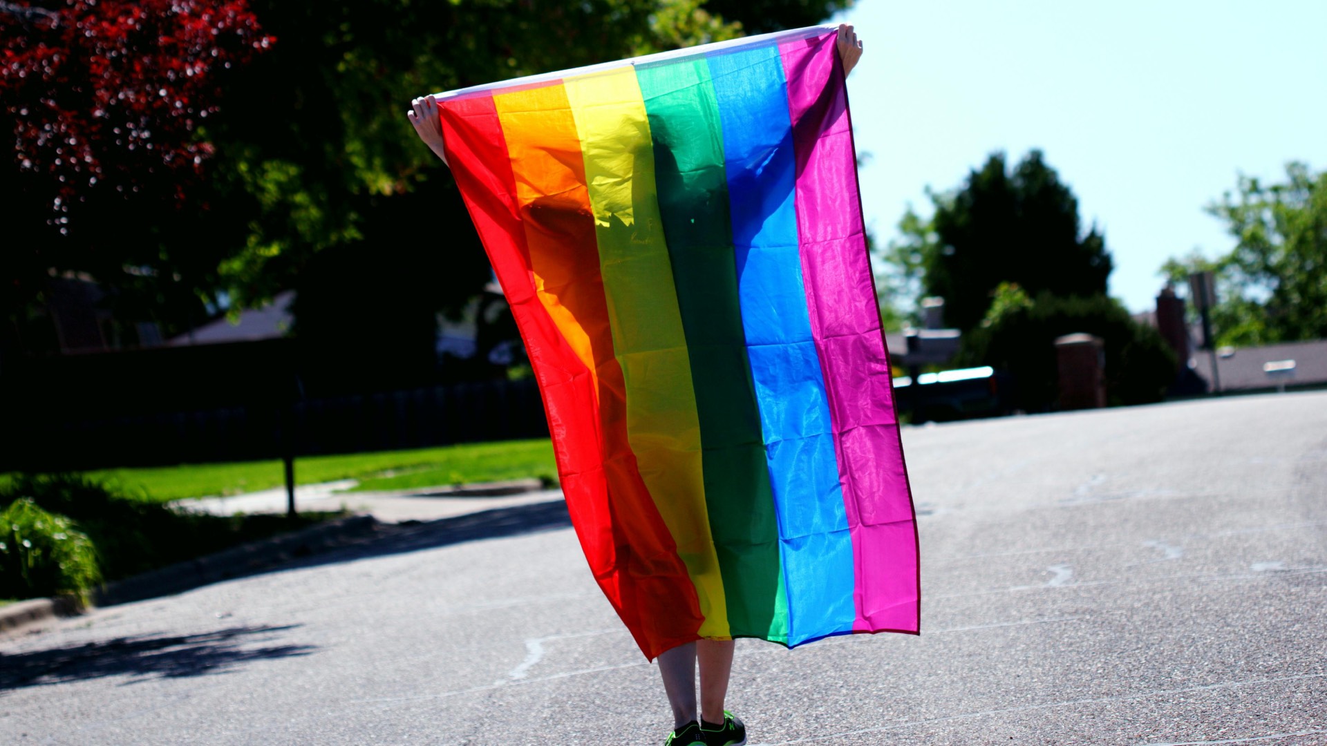 A person walking down a street holding a Pride flag
