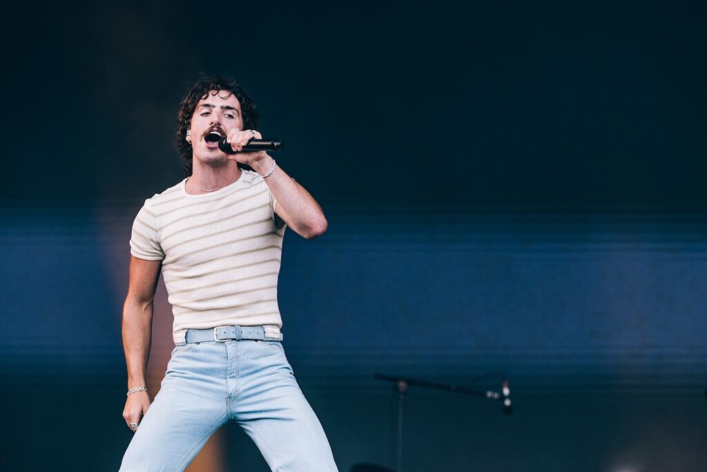 Benson Boone in a white striped t-short and jeans, singing into a mic