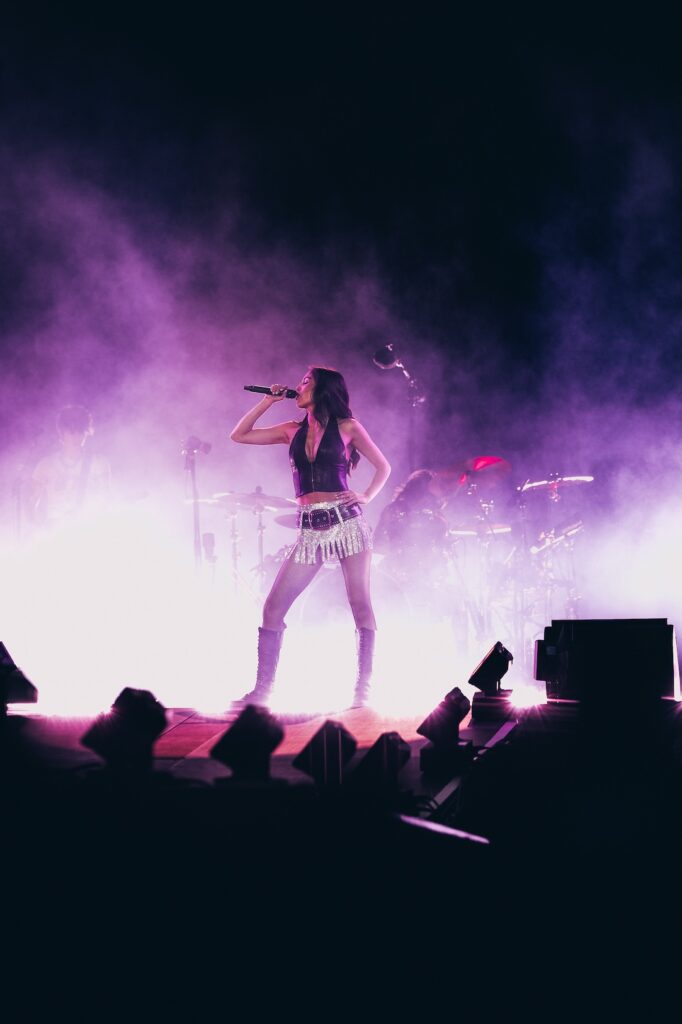 a portrait shaped shot of Olivia holding a mic to her mouth on stage