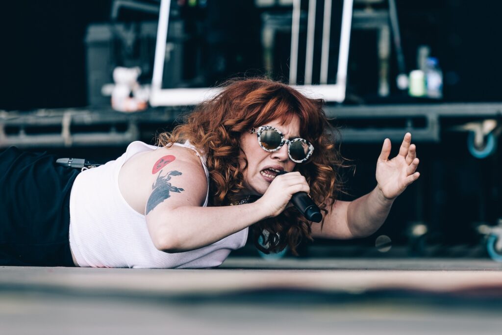 cmat in sunglasses and white vest lying on stage singing