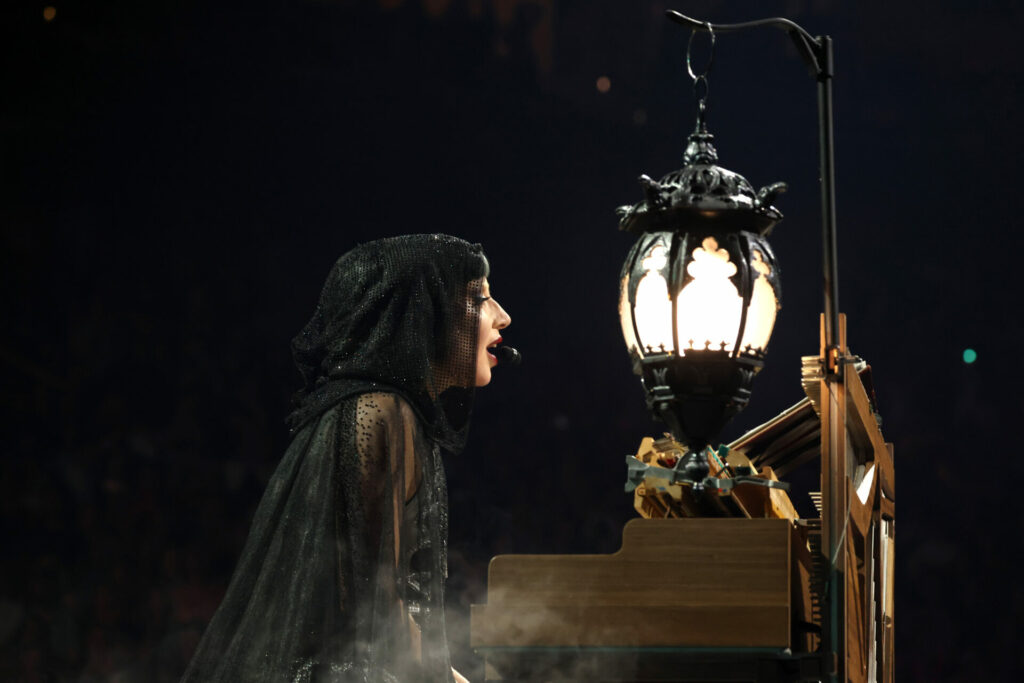 Lady Gaga wearing a hooded cape staring at a hanging lantern