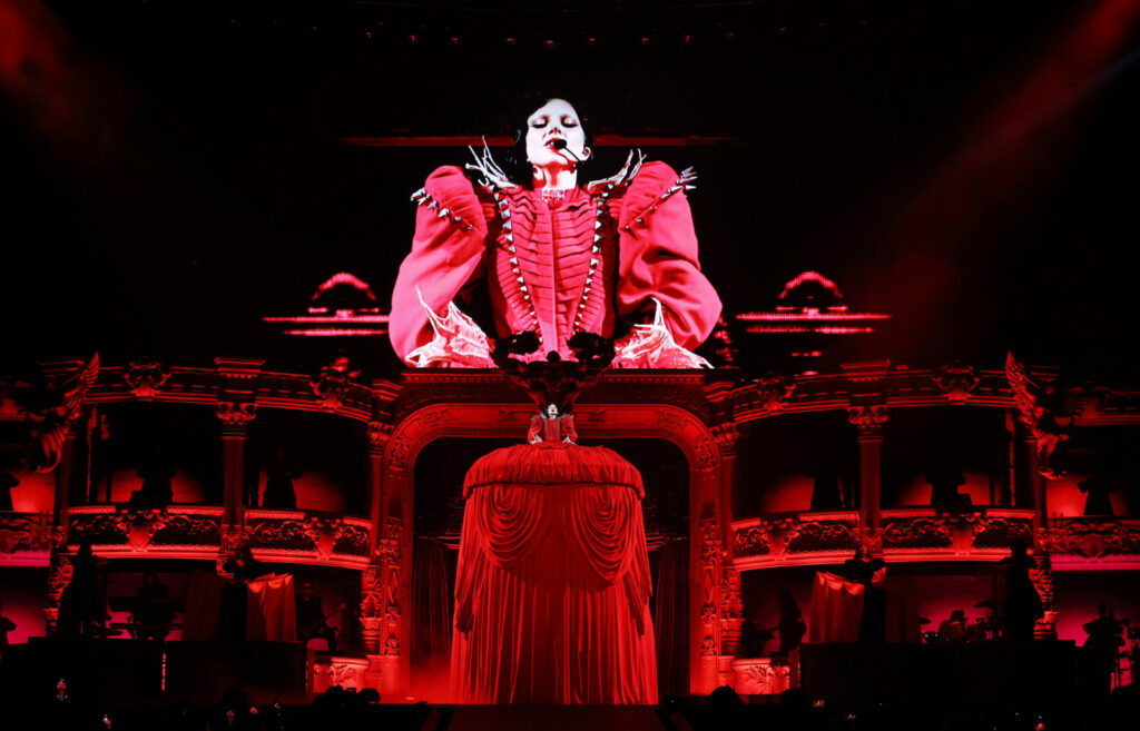 An enlarged lady gaga hollogram dressed in red wearing a black wig