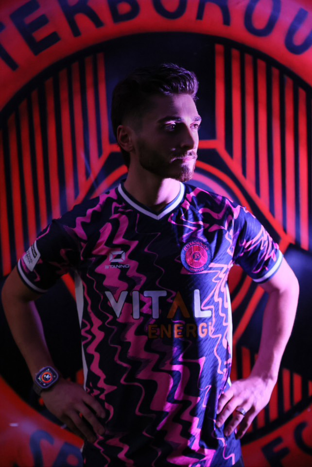 Josh Cavallo in dark pink lighting wearing his Peterborough away uniform