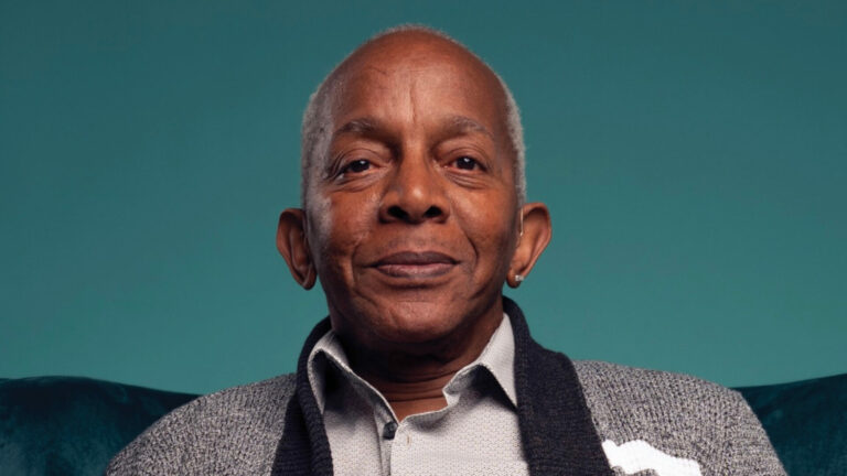Ted Brown in a shirt and cardigan with a turquoise backdrop