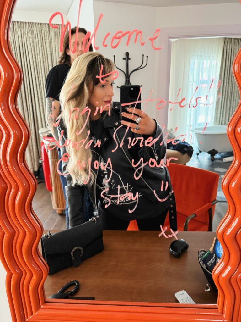 A person taking a photo of themselves in a mirror covered in a lipstick message