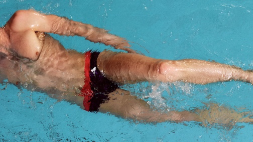 Man swimming front crawl in red and black swimming briefs