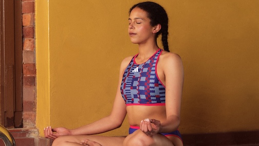 Woman meditating in colourful swim wear against a yellow wall