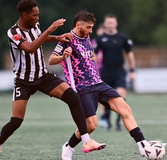 Josh Cavallo playing football in his Peterborough kit beside an opposing player