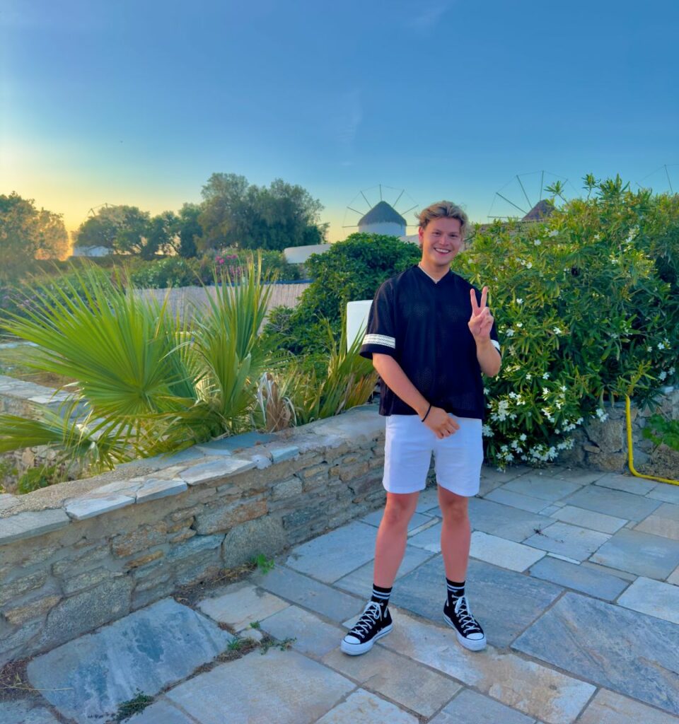 A smiling man in shorts and T-shirt stands in front a rural backdrop