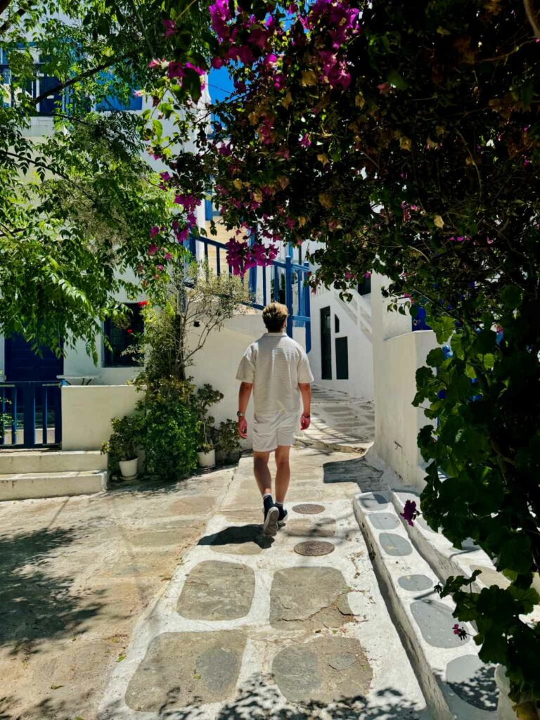 Rear shot of a man in white clothing walking through an ancient Greek town