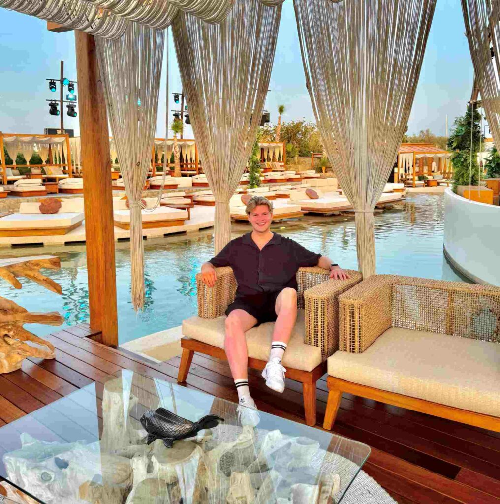 A smiling man in shorts sitting on a sun lounger by a hotel pool