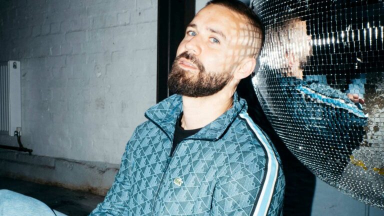 A man wearing a blue tracksuit jacket sitting on the ground resting his head on a disco ball