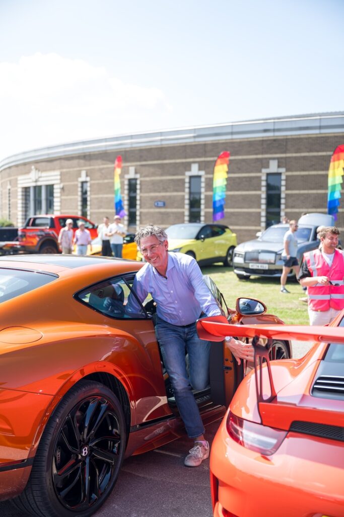 Man getting out of an orange car with pride flags waving in the background 