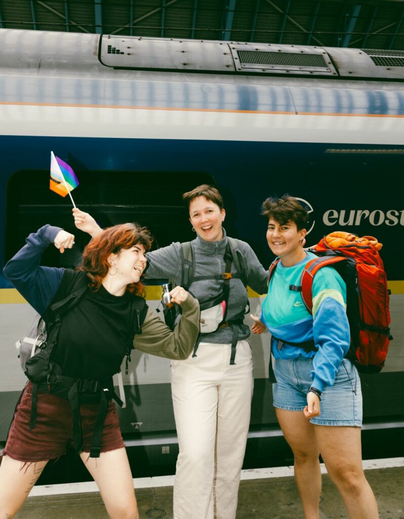 Three smiling people in backpacking gear standing in front of a Eurostar train